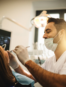 Male with a mask holding a dental tool in woman's mouth