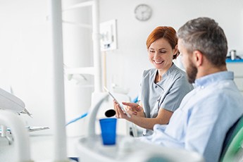 Smiling dentist reviewing information on tablet with patient