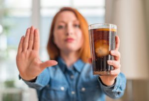 woman with red hair holding a soda in one hand and making a stop signal with the other hand